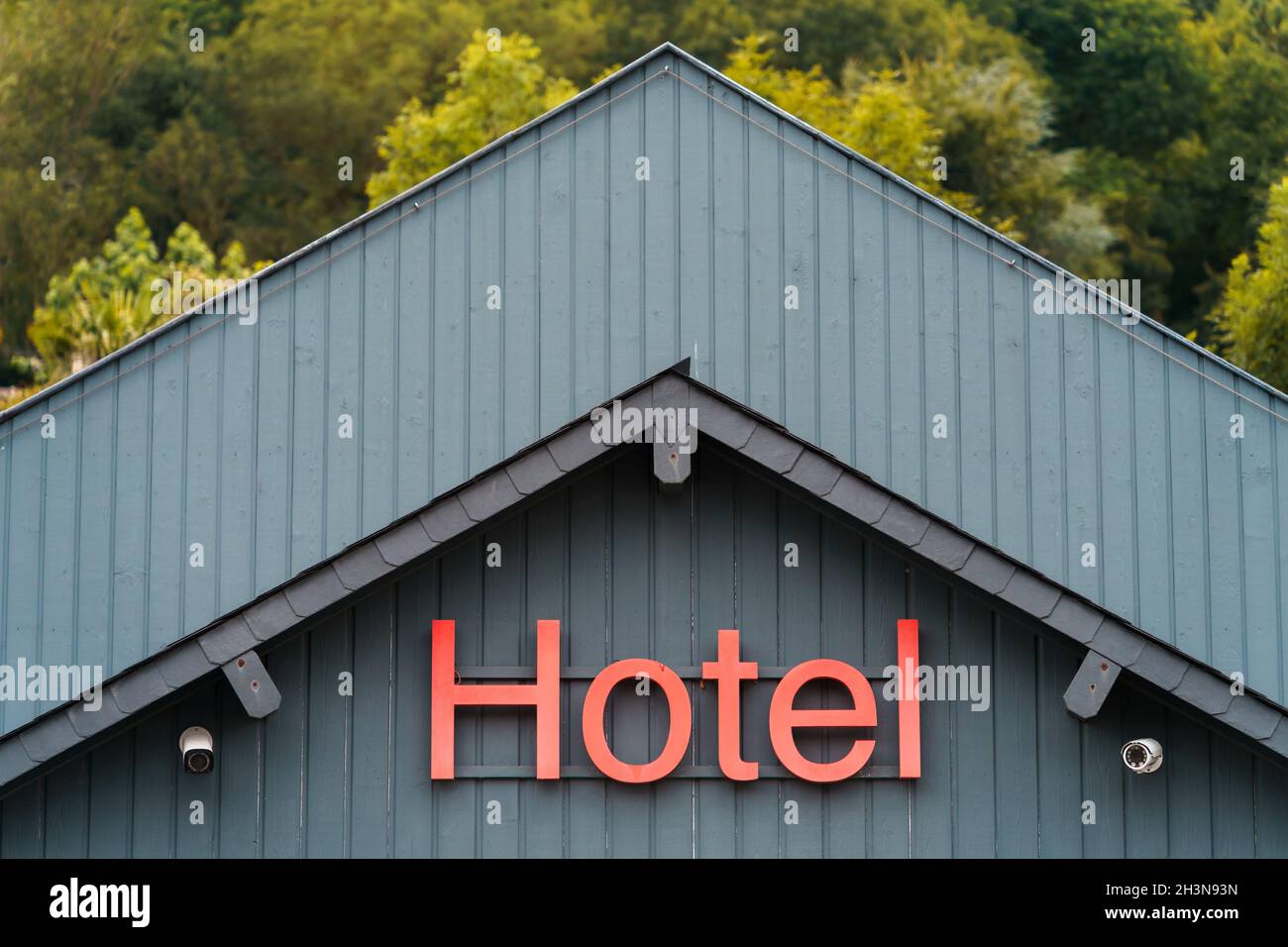 Segno di un hotel su una facciata grigia su un edificio e un legno dietro l'edificio Foto Stock