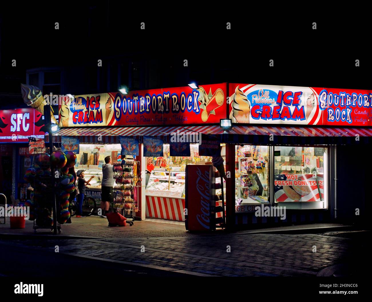 Persone che acquistano dolciumi di notte presso il negozio di roccia a Southport Merseyside Foto Stock