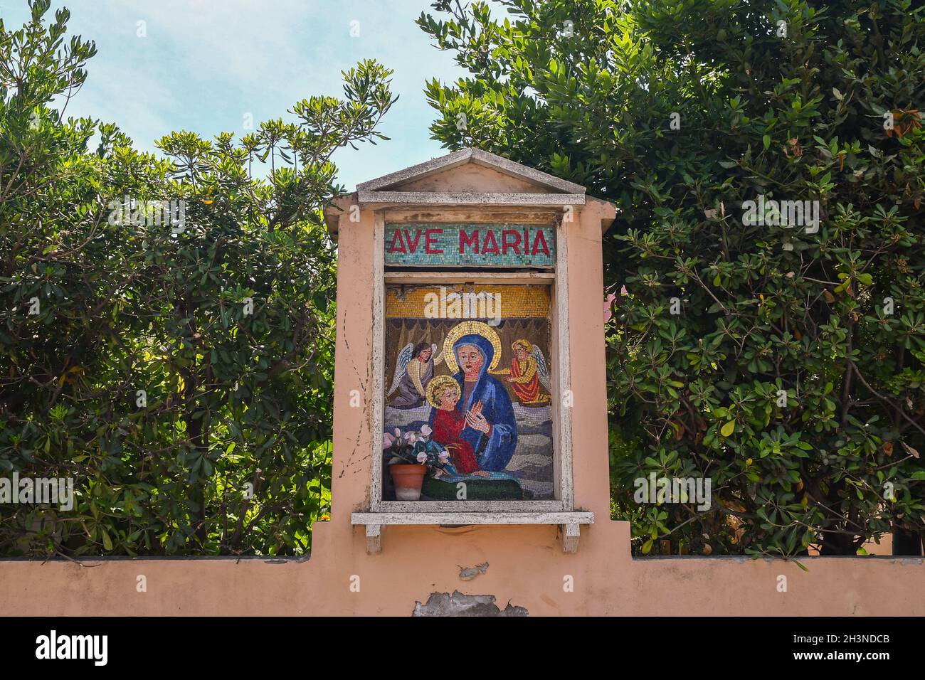 Colorato santuario a mosaico raffigurante Santa Maria con Gesù Bambino sulla parete che racchiude un giardino con piante rigogliose in estate, San Vincenzo, Livorno Foto Stock