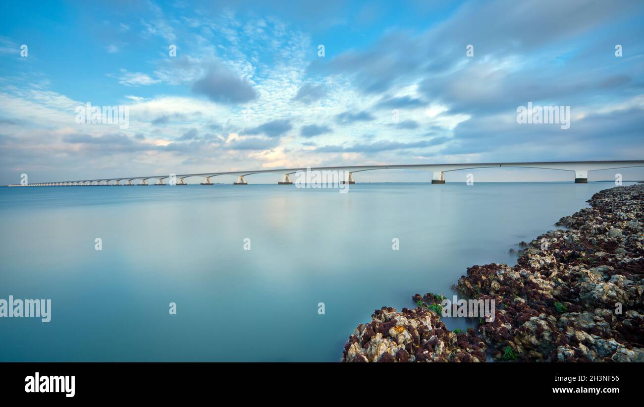Lungo ponte su acque glassose e fluide che va all'infinito sopra il magnifico oceano sotto il bellissimo cielo colorato in Zeeland, Paesi Bassi Foto Stock