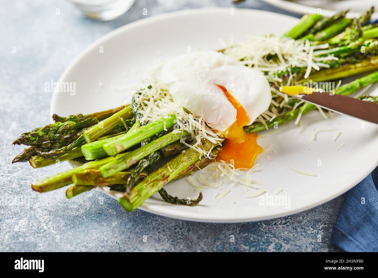 Asparagi verdi con uova in camicia e parmigiano, colazione vegetariana servita su due piatti bianchi su sfondo chiaro. Foto Stock