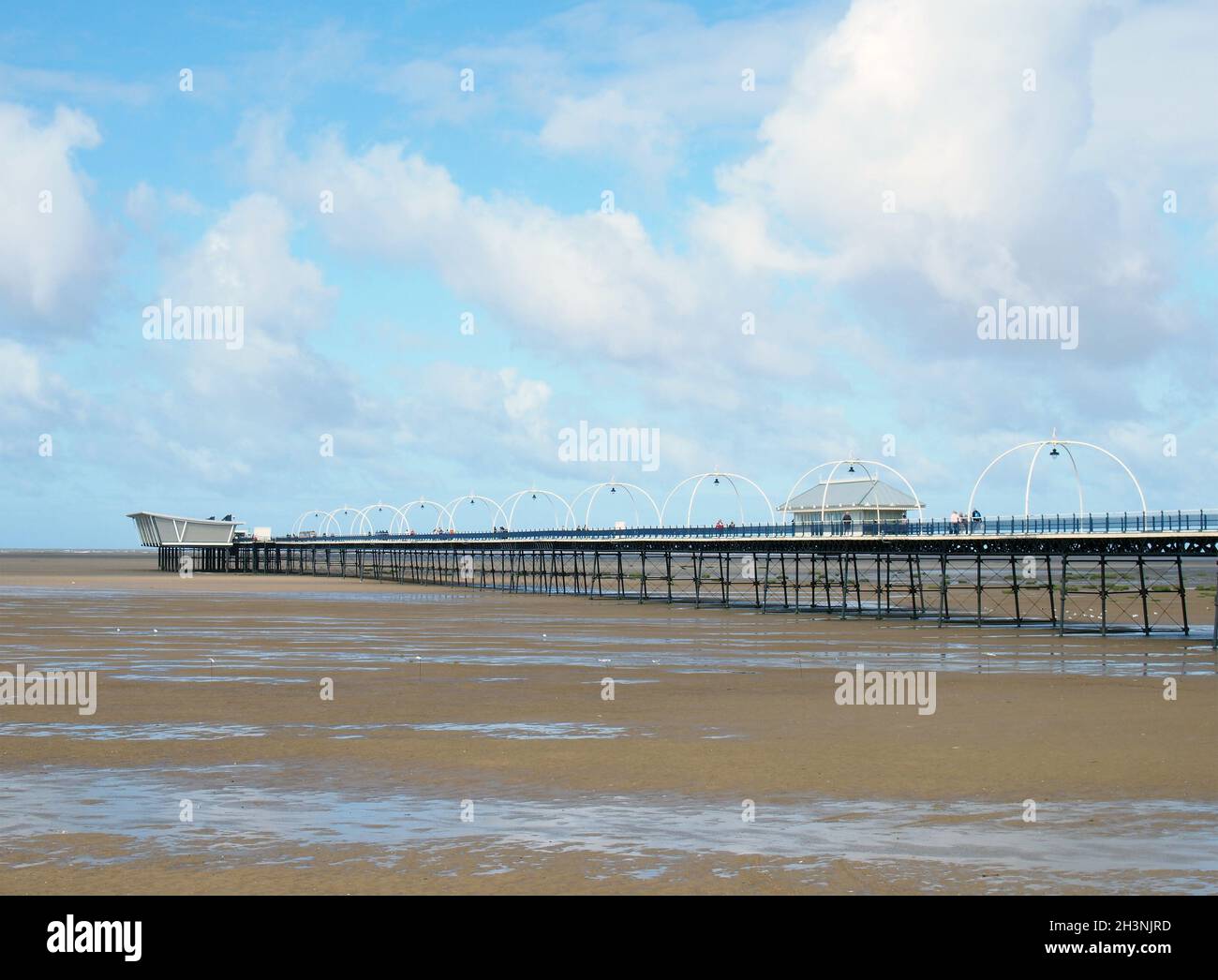 Lo storico molo di southport merseyside con la spiaggia a bassa marea e il cielo estivo si riflette nell'acqua sulla spiaggia Foto Stock