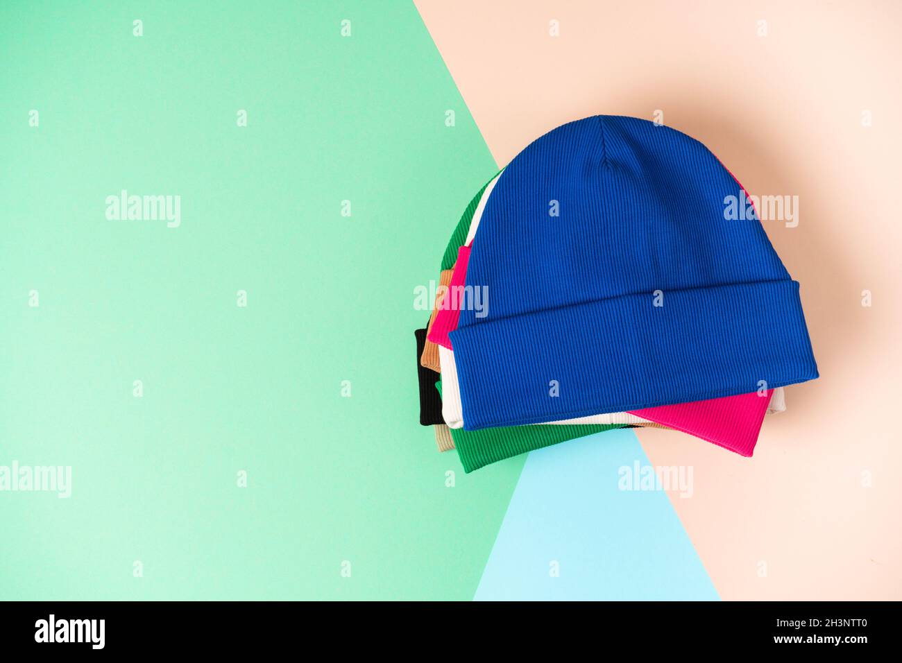 Cappelli di beanie assortiti in diversi colori vivaci della gioventù sono impilati su un delicato sfondo colorato con spazio per il testo. Vista dall'alto Foto Stock