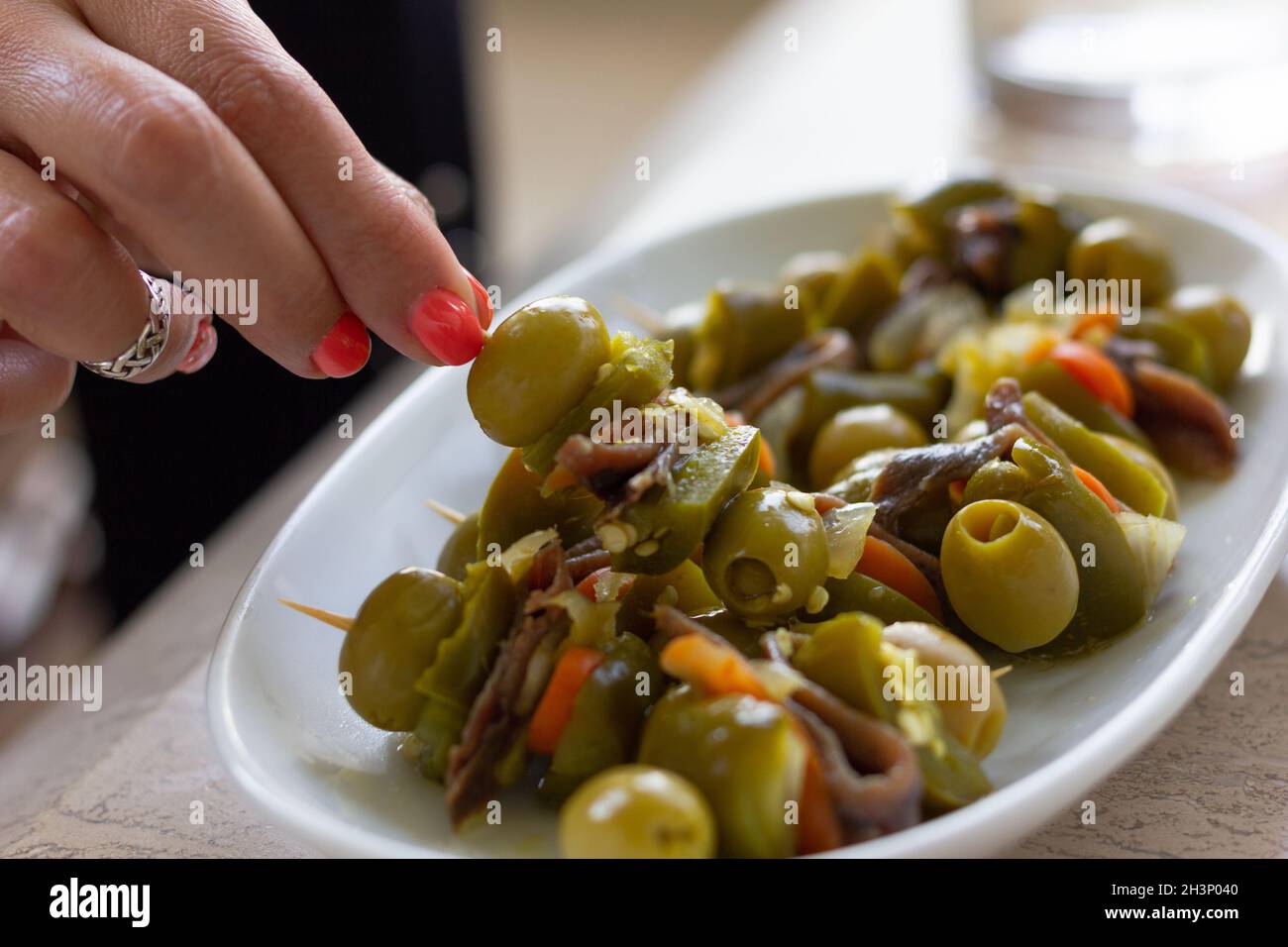 Mano di donna che prende gli antipasti speziati con olive verdi, acciughe e jalapeños. Tradizionale snack basco gildas Foto Stock