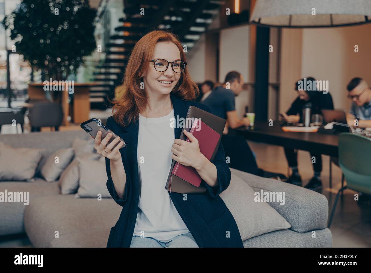 Una donna felice in attesa che la collega arrivi mentre si siede sul divano in ufficio Foto Stock