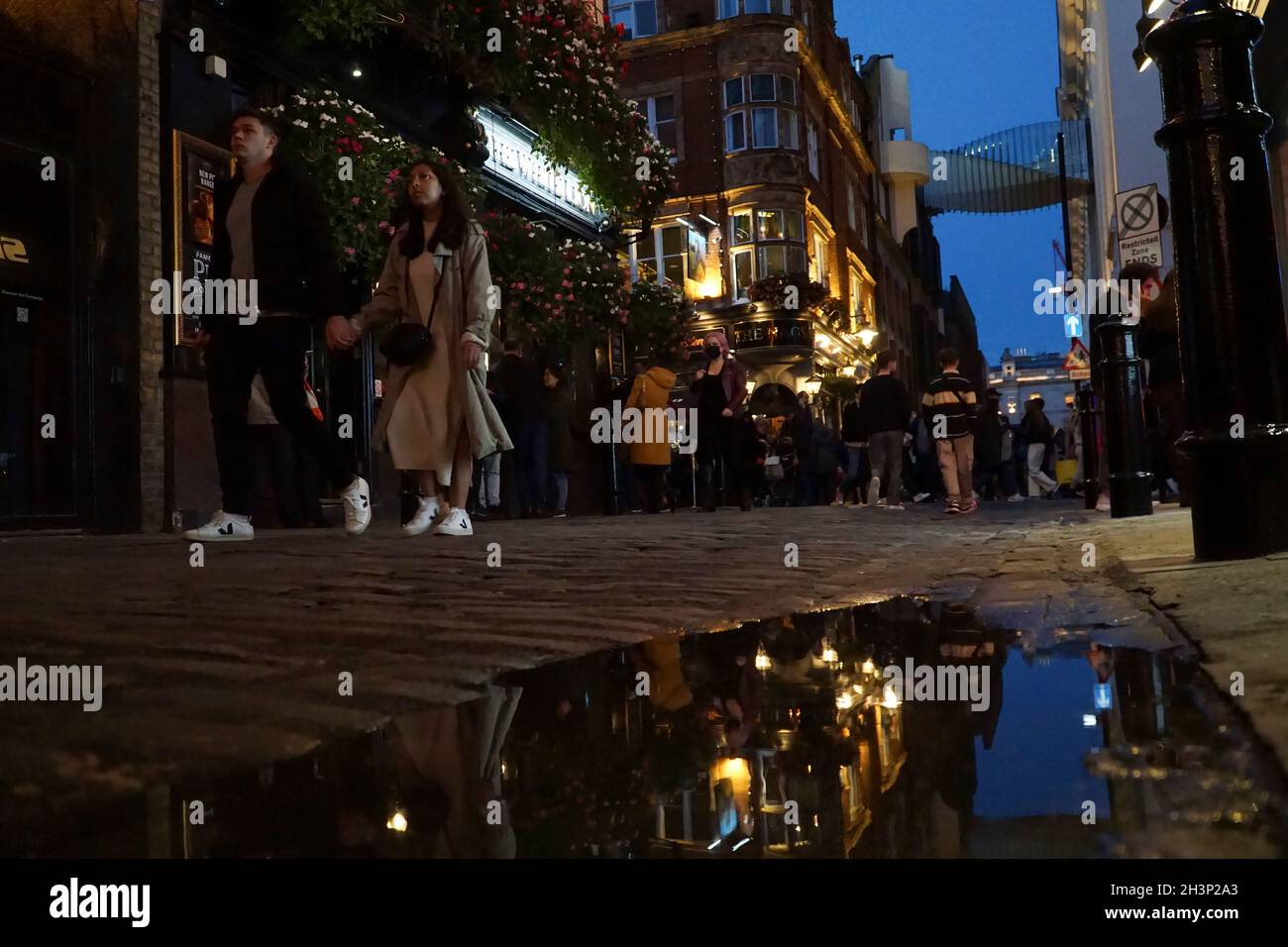 Londra, UK, 29 ottobre 2021: Mentre il crepuscolo cade a Covent Garden e nelle strade acciottolate circostanti, i turisti e gli amanti dello shopping godono di un incantesimo secco tra le docce a pioggia. I ristoranti e i ristoratori di bar, pub o ristoranti hanno spesso la scelta di sedersi all'interno o all'esterno. Le campagne pubblicitarie volte a incoraggiare le persone a visitare Londra sembrano aver attirato molte visite familiari a metà termine e Londra ha attualmente un tasso di infezioni da covid inferiore rispetto ad altre aree del paese. Le decorazioni natalizie sono già in alto nella zona centrale del mercato. Anna Watson/Alamy Live News Foto Stock