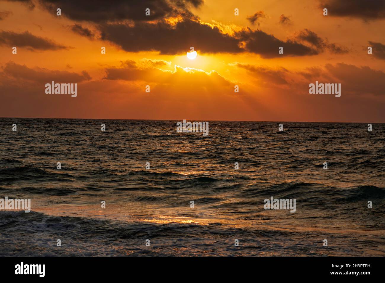Tramonto sul Mar Mediterraneo. I raggi del sole si riflettono attraverso le nuvole nell'acqua. Foto Stock