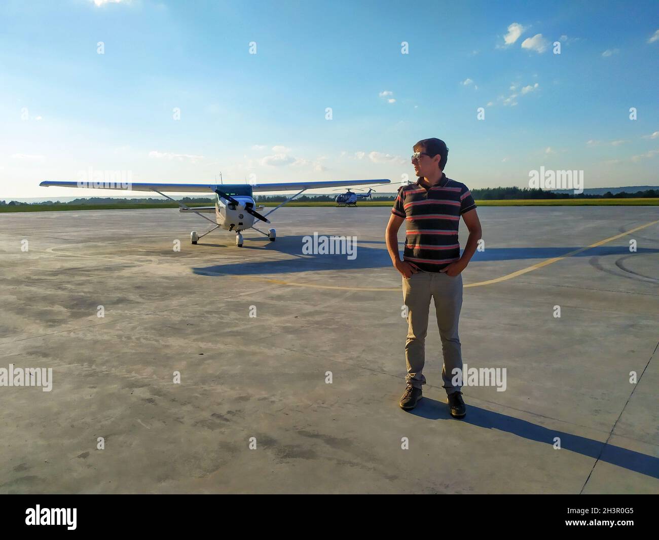 pilota maschile in occhiali in piedi vicino ad un piccolo aereo sul campo d'aria Foto Stock