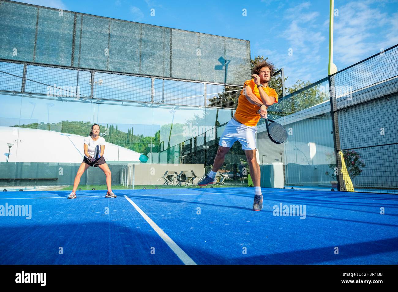 Misto padel match in una corte di erba blu padel - bella ragazza e bell'uomo giocare padel all'aperto Foto Stock