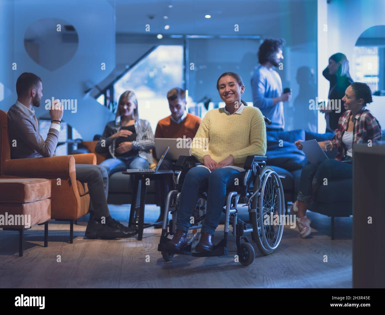 Ritratto di una donna d'affari disabile su una sedia a rotelle di fronte il suo team aziendale in ufficio Foto Stock