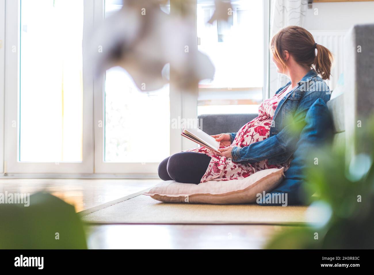 Preparazione per la gravidanza: Gravidanza la madre caucasica è seduta sul pavimento, leggendo un libro per circa i bambini Foto Stock