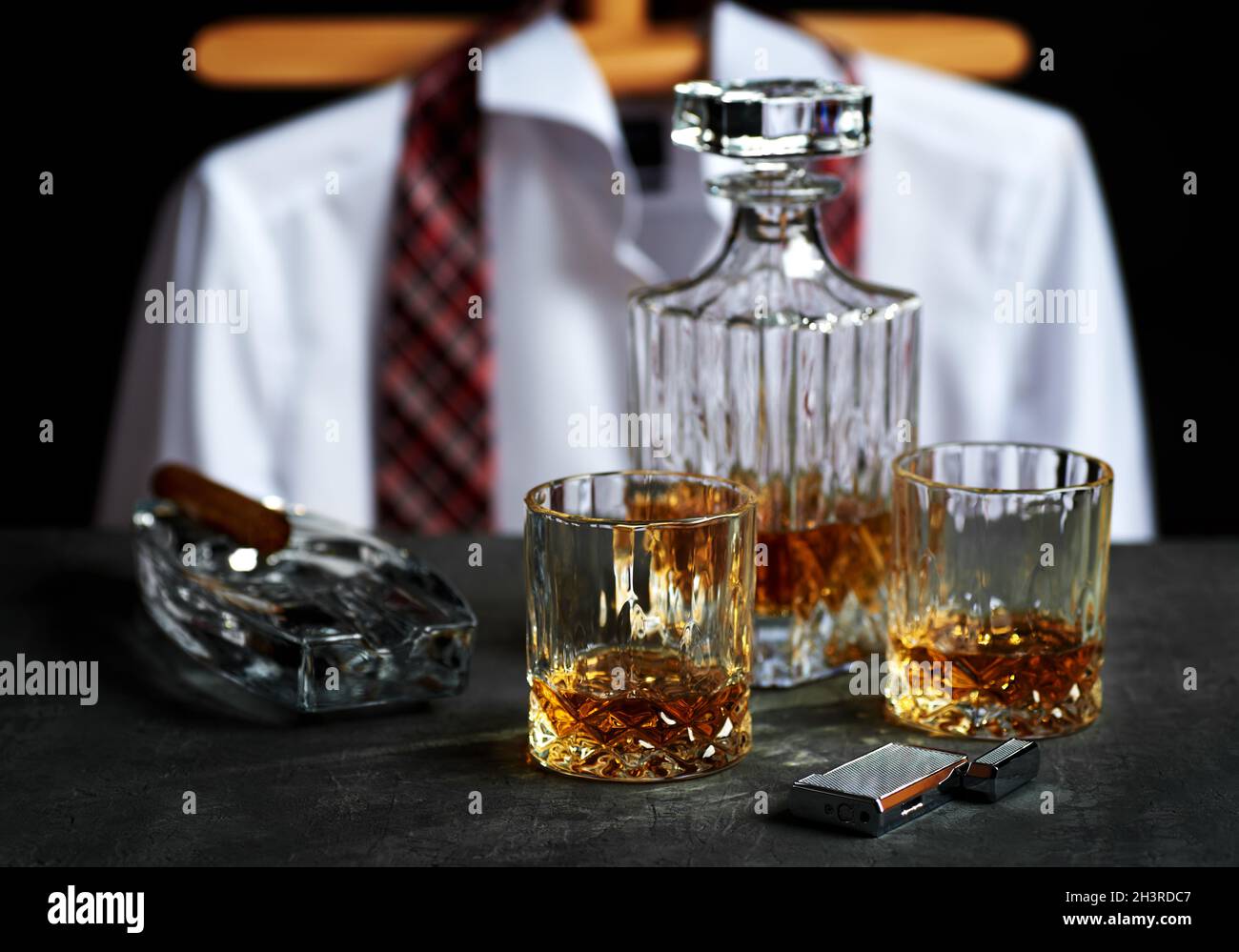 Ancora vita con una bottiglia e due bicchieri di whiskey su un tavolo in pietra in un bar. Accendisigari cubano con camicia bianca e cravatta rossa su bac nero Foto Stock