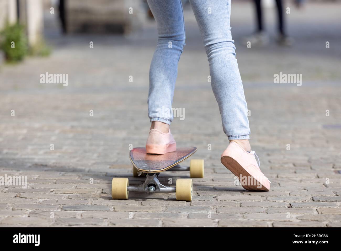 Primo piano di piedi femminili di una ragazza che indossa sneakers rosa e un jeans sullo skateboard sullo sfondo delle strade della città Foto Stock