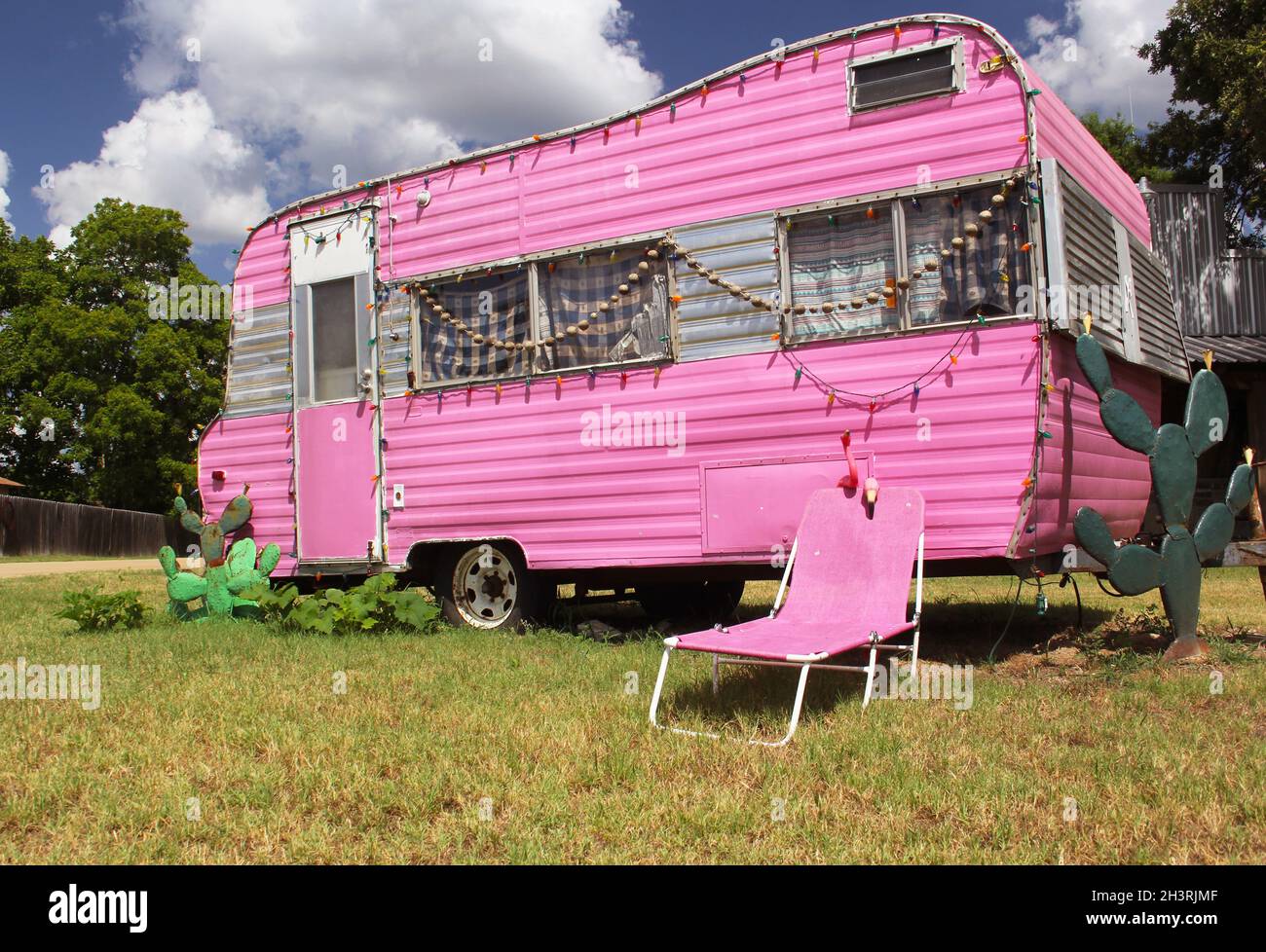 Rimorchio da viaggio rosa con sedia e cactus più cielo blu e nuvole Foto Stock