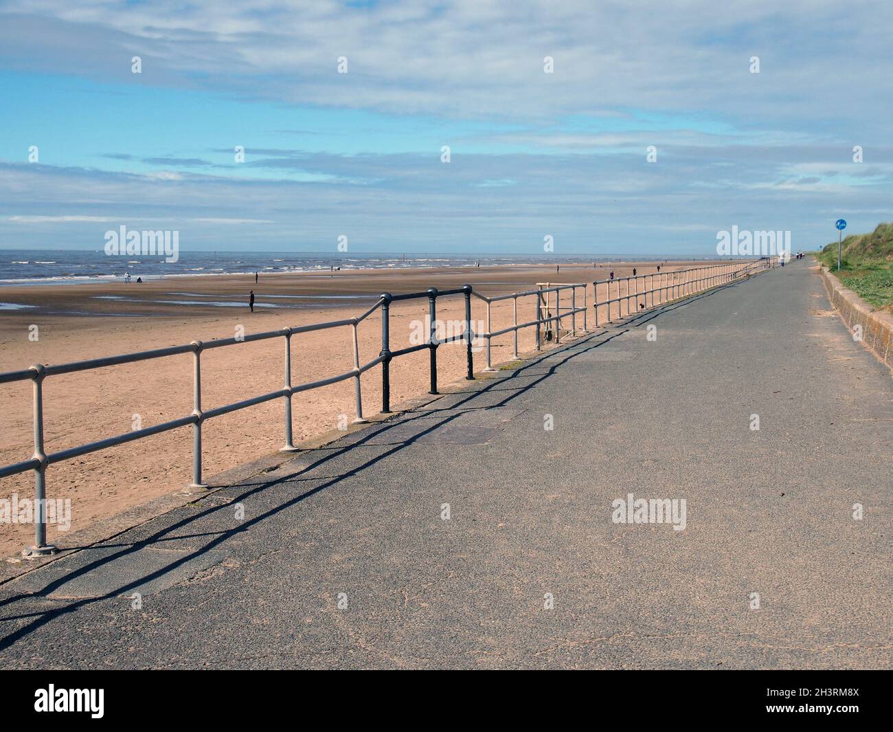 La passerella pedonale accanto al mare in crosby merseyside con figure distanti sulla spiaggia alla luce del sole estivo Foto Stock