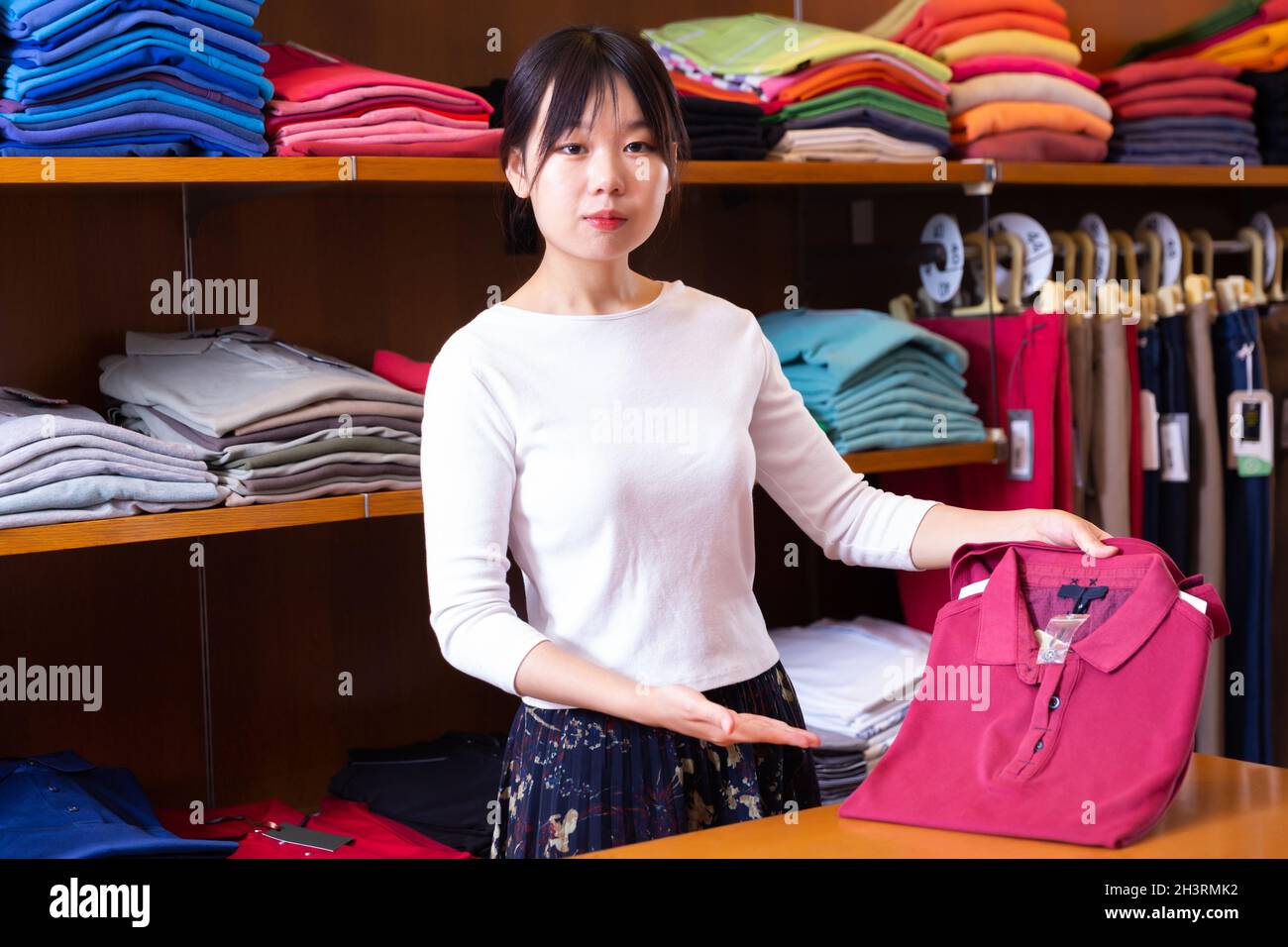 Assistente di shopping femminile cinese che offre varie camicie nel negozio di panni uomo Foto Stock