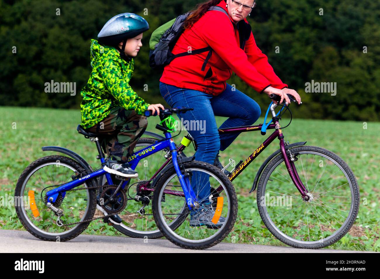 Ragazzo piccolo, bambino in bicicletta in casco, vista laterale con mamma Foto Stock