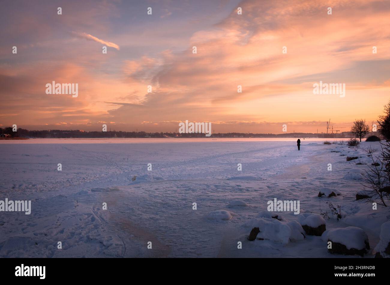 Tramonto invernale sul mare ghiacciato. Una silhouette di una donna che cammina sul ghiaccio. Foto Stock