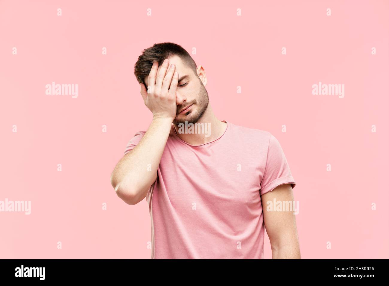 Stanco deluso giovane uomo con viso palmo gesto su sfondo rosa Foto Stock