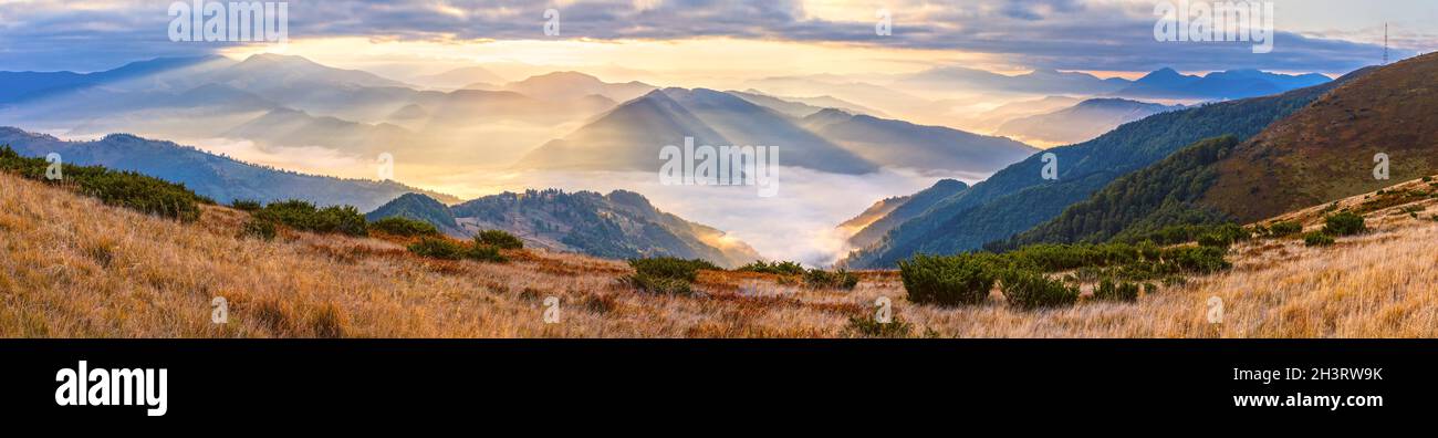 Autunno mattina vista panoramica montagna con travi a vista attraverso foschia e basse nuvole. Foto Stock