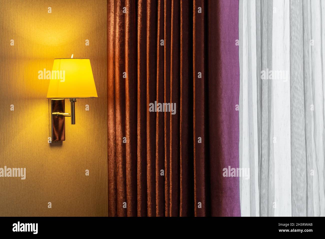 Una combinazione di una moderna parete, una classica tenda a motivi geometrici e una tenda tulle. La spia è accesa. La luce del sole proviene dall'esterno. Foto Stock
