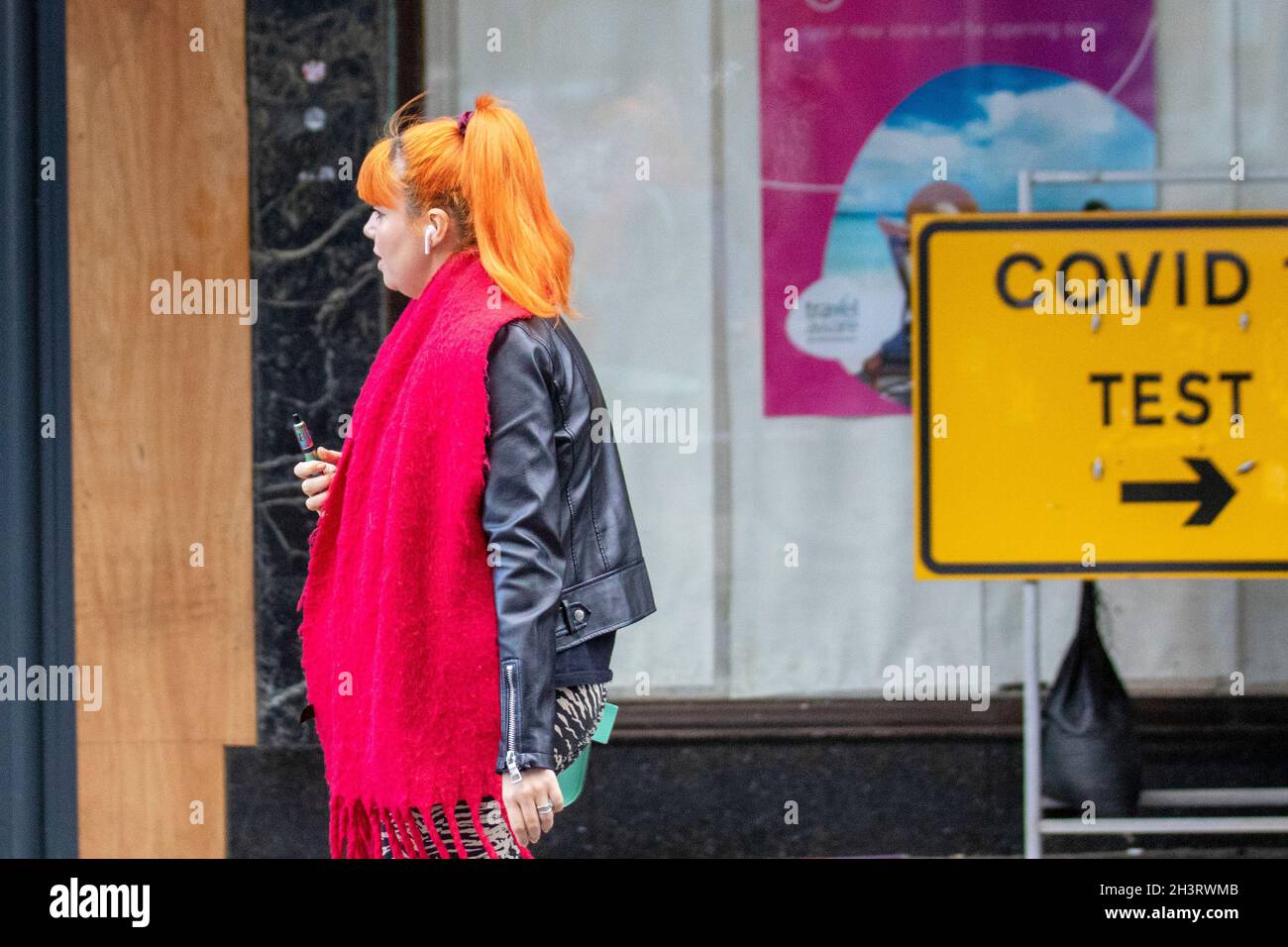 Southport, Merseyside. Meteo UK 30 Ott 2021. Donna con haier rosso e sciarpa che cammina oltre il cartello del centro di riposo Covid 19. Al mattino presto docce pesanti nel resort nord-ovest. Credit; MediaWorldImages/AlamyLiveNews Foto Stock