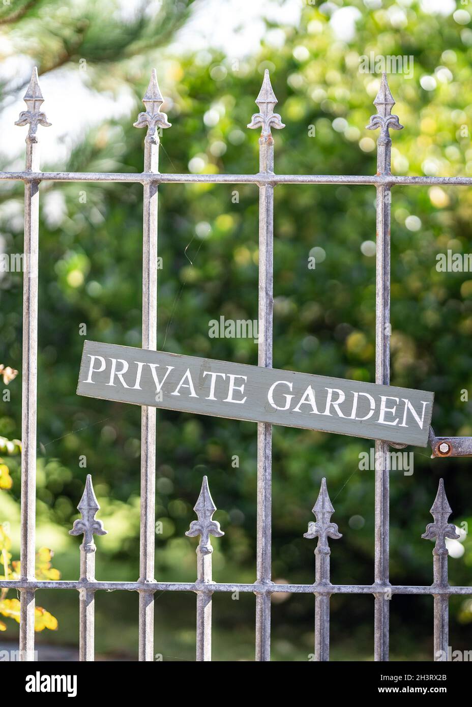 Giardino privato con cancello in metallo e cartello in legno. Tenere fuori messaggio con giardini verdi dietro. Foto Stock