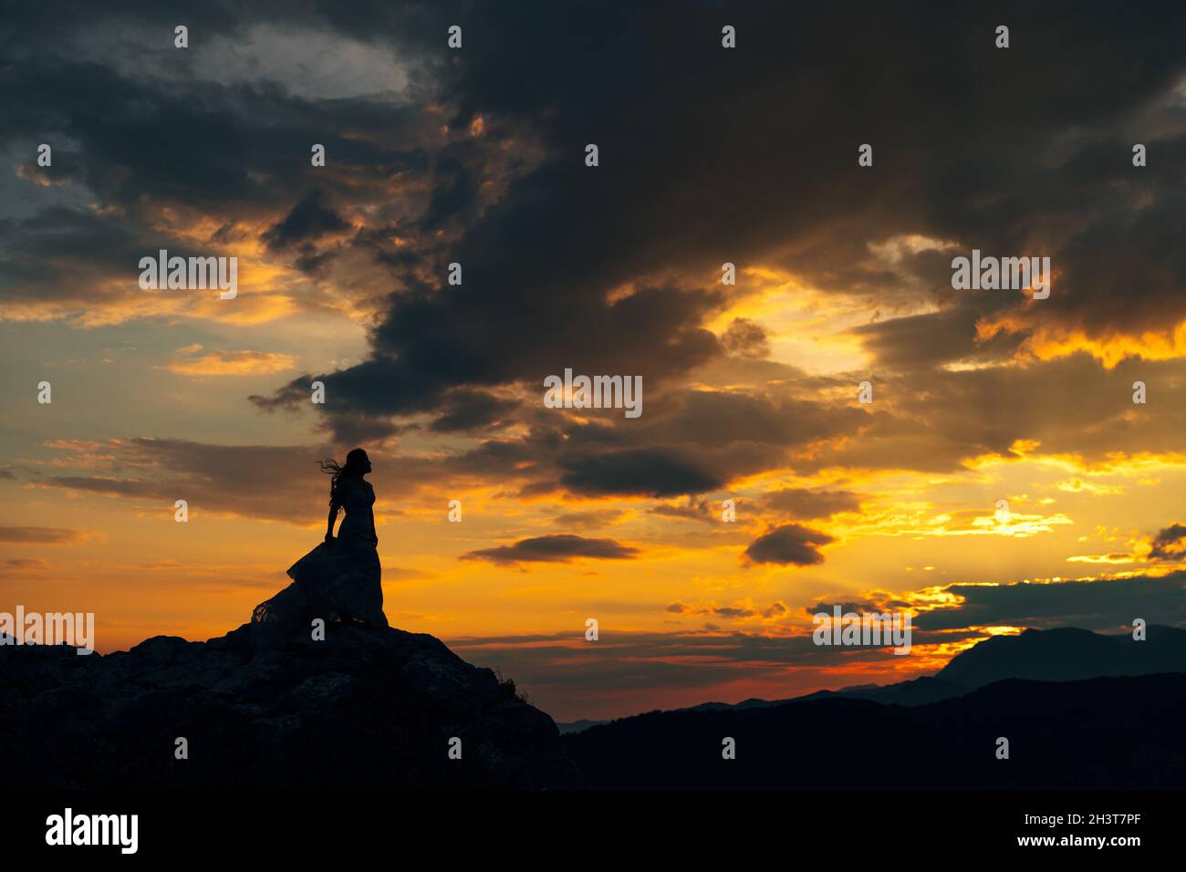 Silhouette della sposa che si erge sulle rocce delle montagne al tramonto Foto Stock