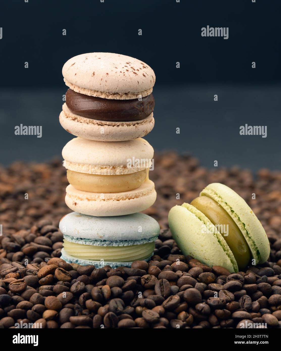 Una pila di macaron multicolore si trova su chicchi di caffè tostati, sfondo nero Foto Stock