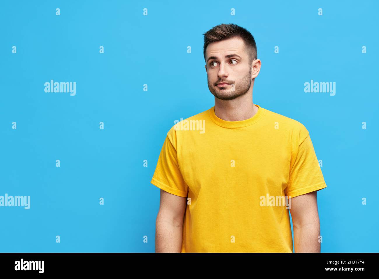 Uomo dubbioso e premuroso che guarda da parte per copiare lo spazio su sfondo blu Foto Stock