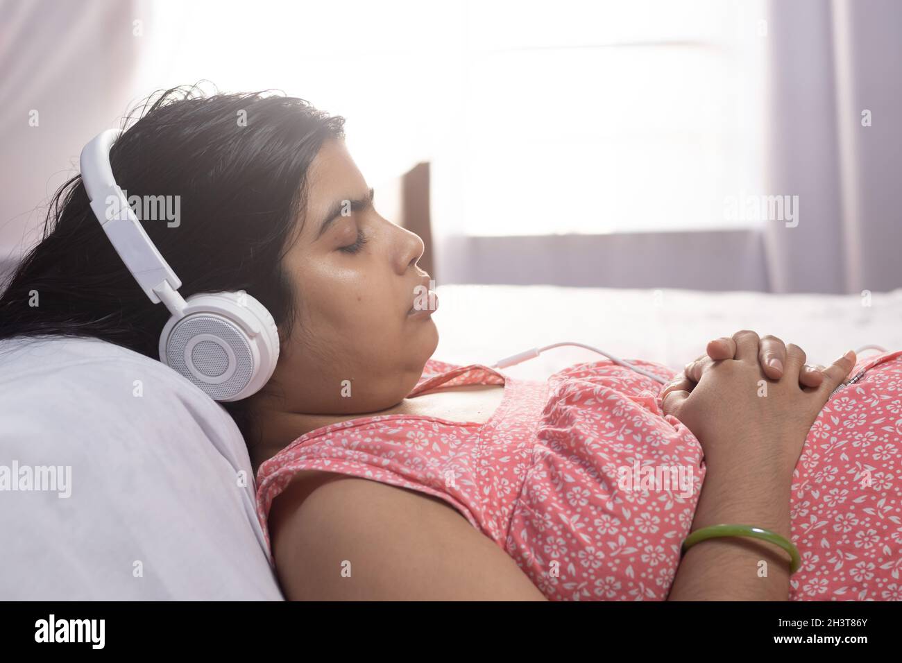 Una donna indiana asiatica che dorme a letto mentre ascolti la musica in cuffia Foto Stock