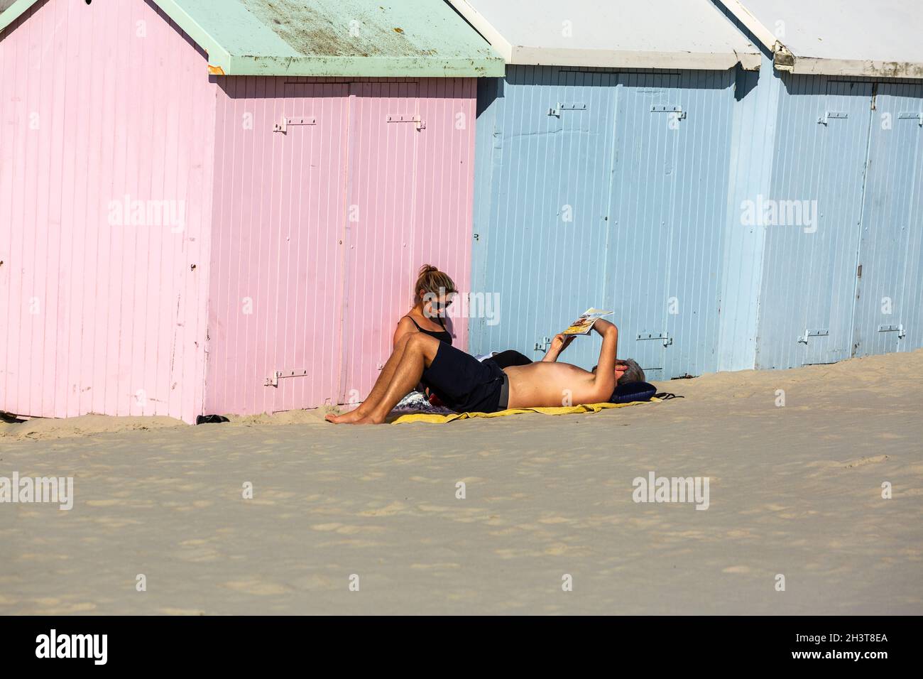 Coppia crogiolarsi al sole da colorate capanne sulla spiaggia. Berck-Plage, Costa d'Opale, Francia Foto Stock