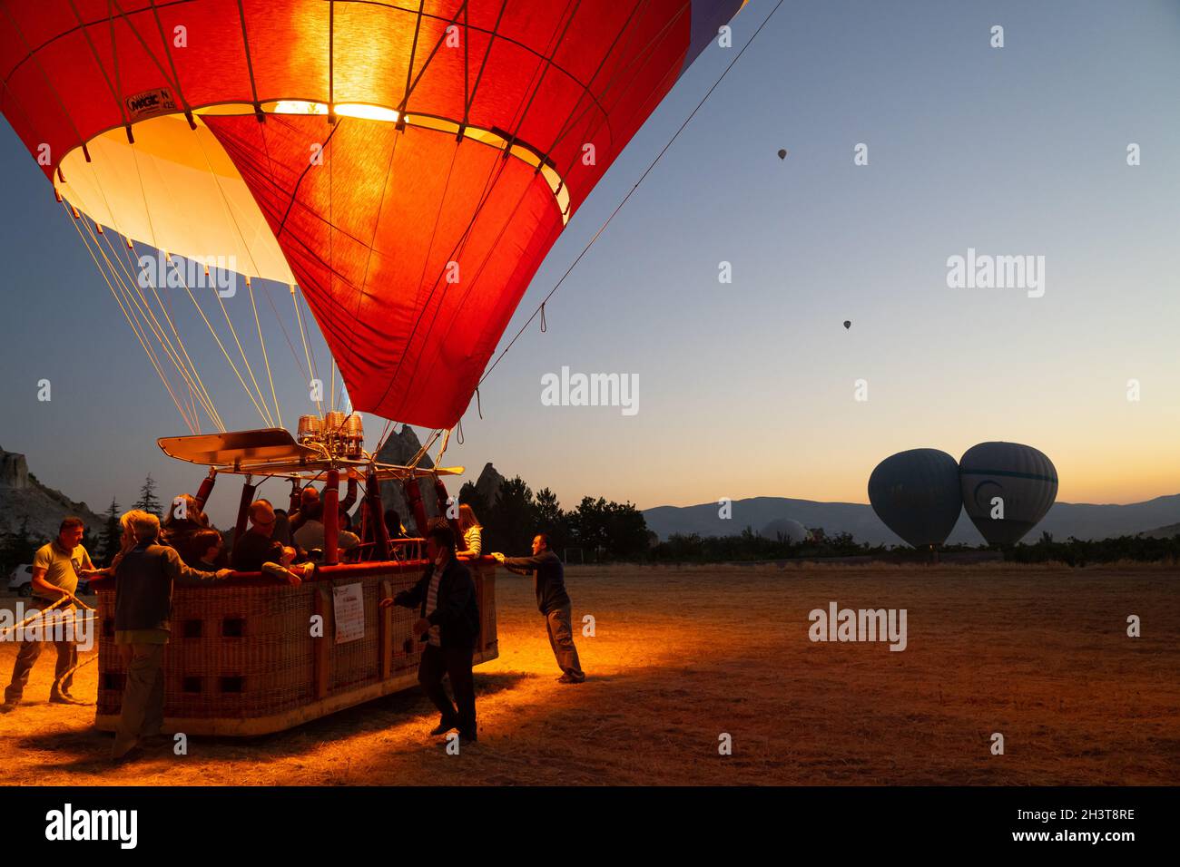 GOREME, TURCHIA - 3 AGOSTO 2021: Persone posizione per decollo di un pallone ad aria calda pieno di turisti, mentre il capitano accende il bruciatore fiamma an Foto Stock