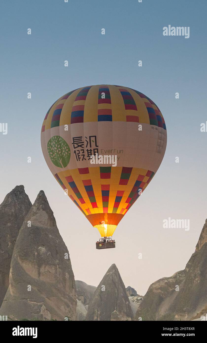 GOREME, TURCHIA - 5 AGOSTO 2021: Mongolfiera con turisti che sparano la sua fiamma bruciatore e volare basso vicino alle case delle caverne dei camini fairy a Cappado Foto Stock