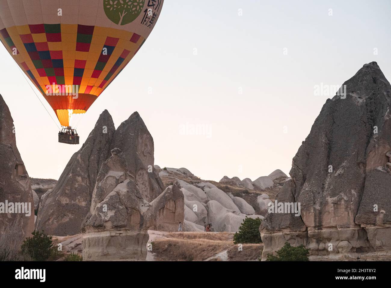 GOREME, TURCHIA - 5 AGOSTO 2021: Mongolfiera con turisti che sparano la sua fiamma bruciatore e volare basso vicino alle case delle caverne dei camini fairy a Cappado Foto Stock