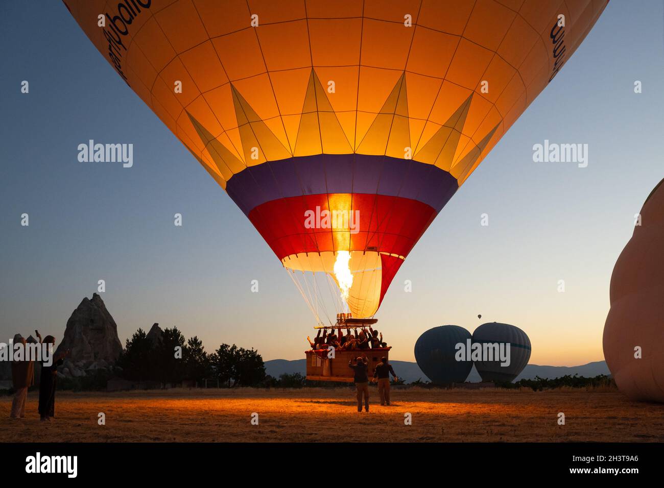GOREME, TURCHIA - 3 AGOSTO 2021: Persone posizione per decollo di un pallone ad aria calda pieno di turisti, mentre il capitano accende il bruciatore fiamma an Foto Stock