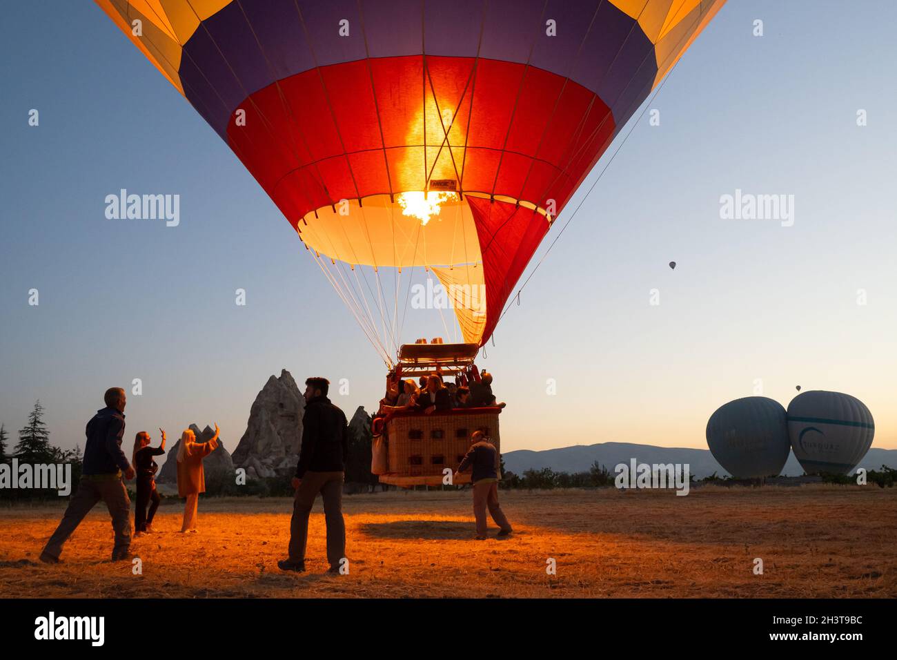 GOREME, TURCHIA - 3 AGOSTO 2021: Persone posizione per decollo di un pallone ad aria calda pieno di turisti, mentre il capitano accende il bruciatore fiamma an Foto Stock