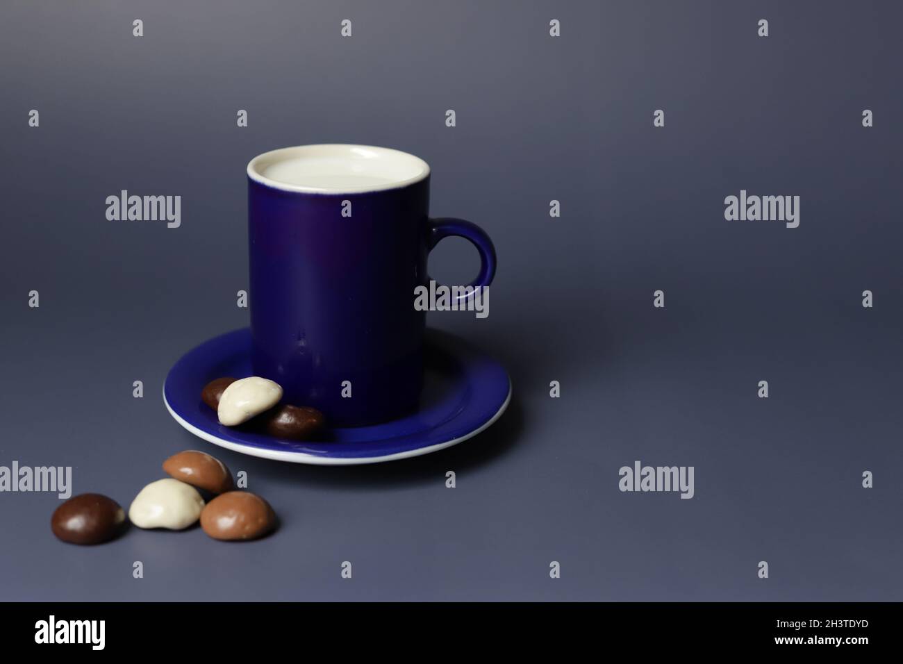 Tazza blu con latte e piccolo piatto blu con biscotti al cioccolato per la colazione la mattina. Foto di alta qualità Foto Stock