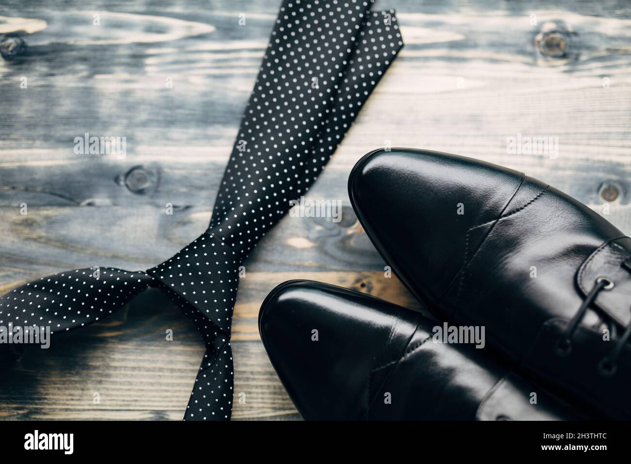 Cravatta nera con puntini bianchi in polka e scarpe da uomo in pelle su sfondo in legno. Foto Stock