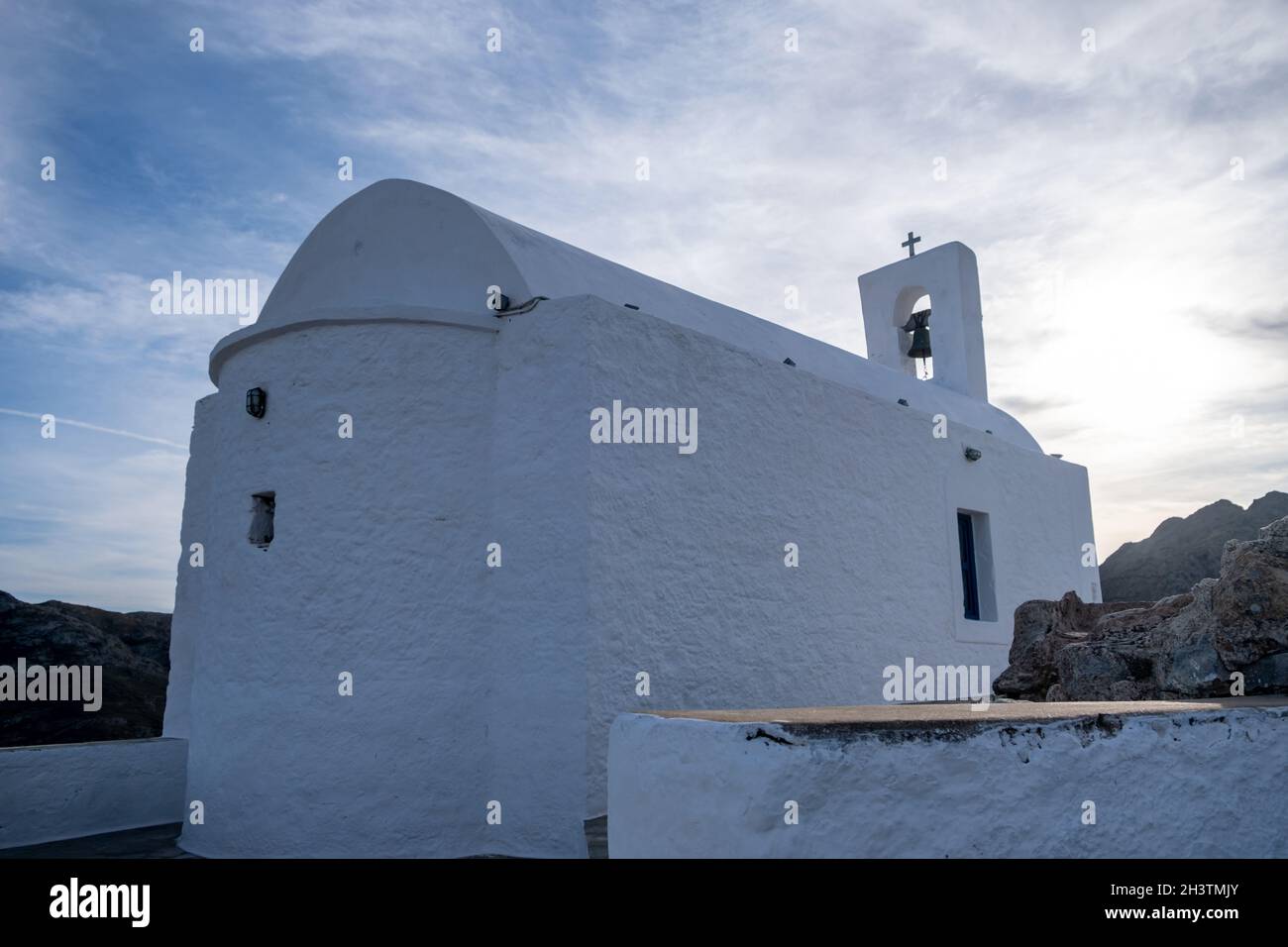 Isola di Serifos, Grecia. Piccola cappella antica, pareti bianche e campanile, chiesa greca ortodossa sulla collina rocciosa, cielo blu nuvoloso sfondo. Foto Stock