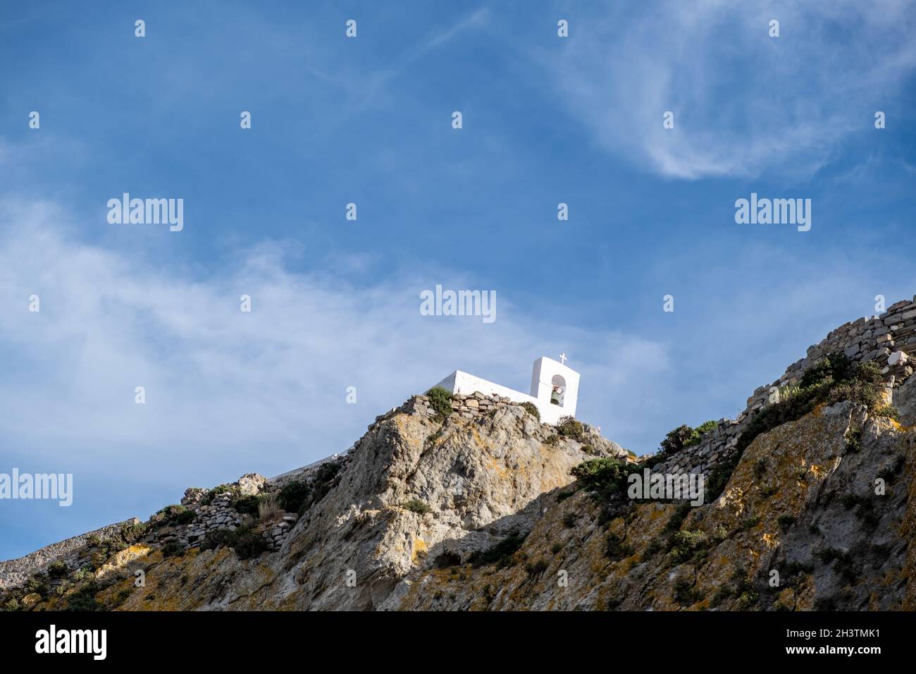 Piccola cappella antica, pareti bianche e campanile, chiesa greca ortodossa sulla collina rocciosa, cielo blu sfondo. Isola di Serifos, Grecia Foto Stock