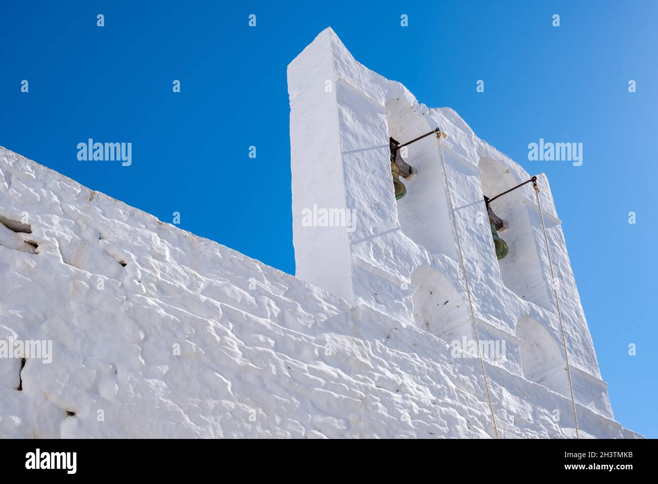 Campanile della Chiesa Ortodossa bianca con due campane. Parete bianca sullo sfondo blu chiaro del cielo. Isola di Sifnos, Cicladi Grecia. Foto Stock