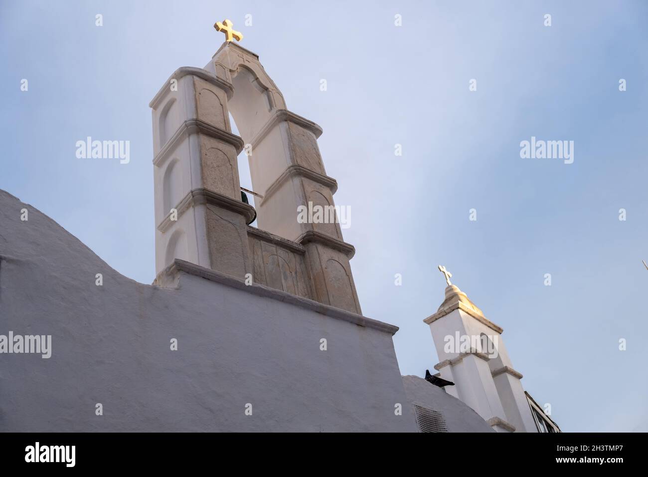 Campanili della chiesa ortodossa bianca con croce d'oro. Muro imbiancato sullo sfondo blu del cielo. Isola di Mykonos, Cicladi Grecia. Foto Stock