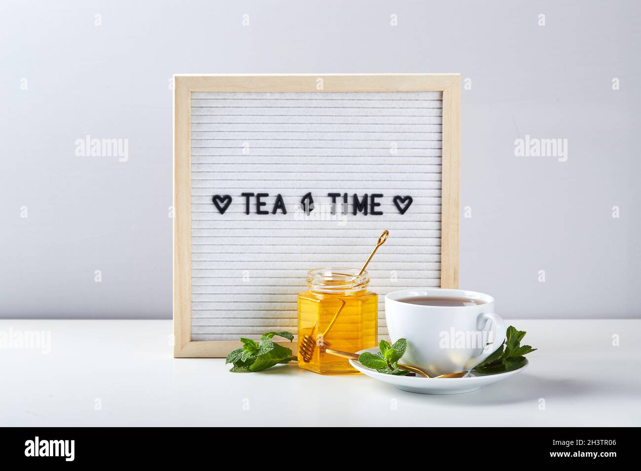 Ora del tè. Lavagna bianca con testo su tavolo di marmo con tazza di tè in vetro con foglie di menta Foto Stock