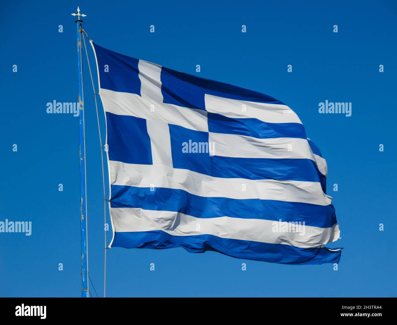 La bandiera nazionale della Grecia sul pennone si sviluppa nel vento contro il cielo blu Foto Stock