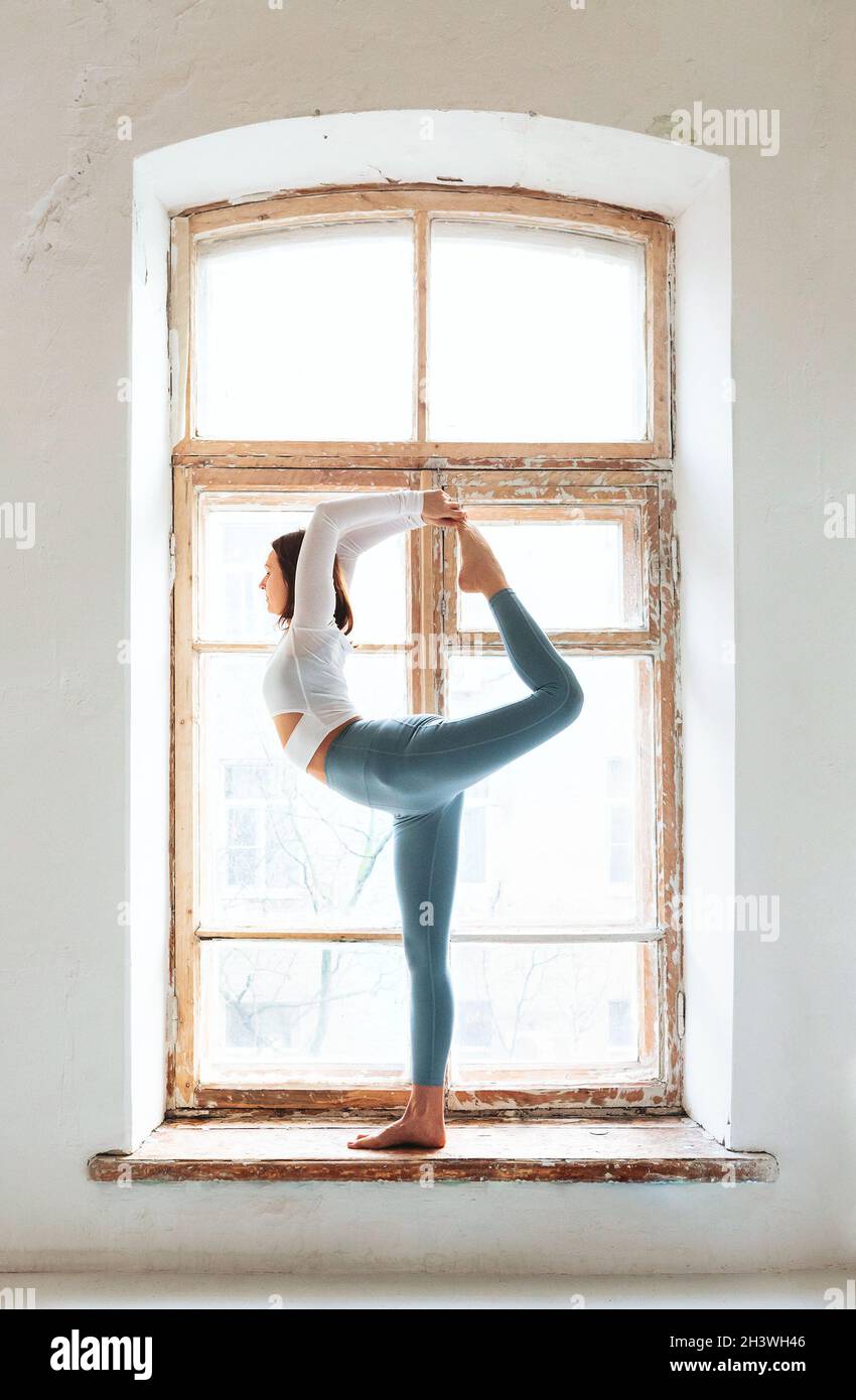 Donna che fa yoga vicino alla finestra shabby Foto Stock