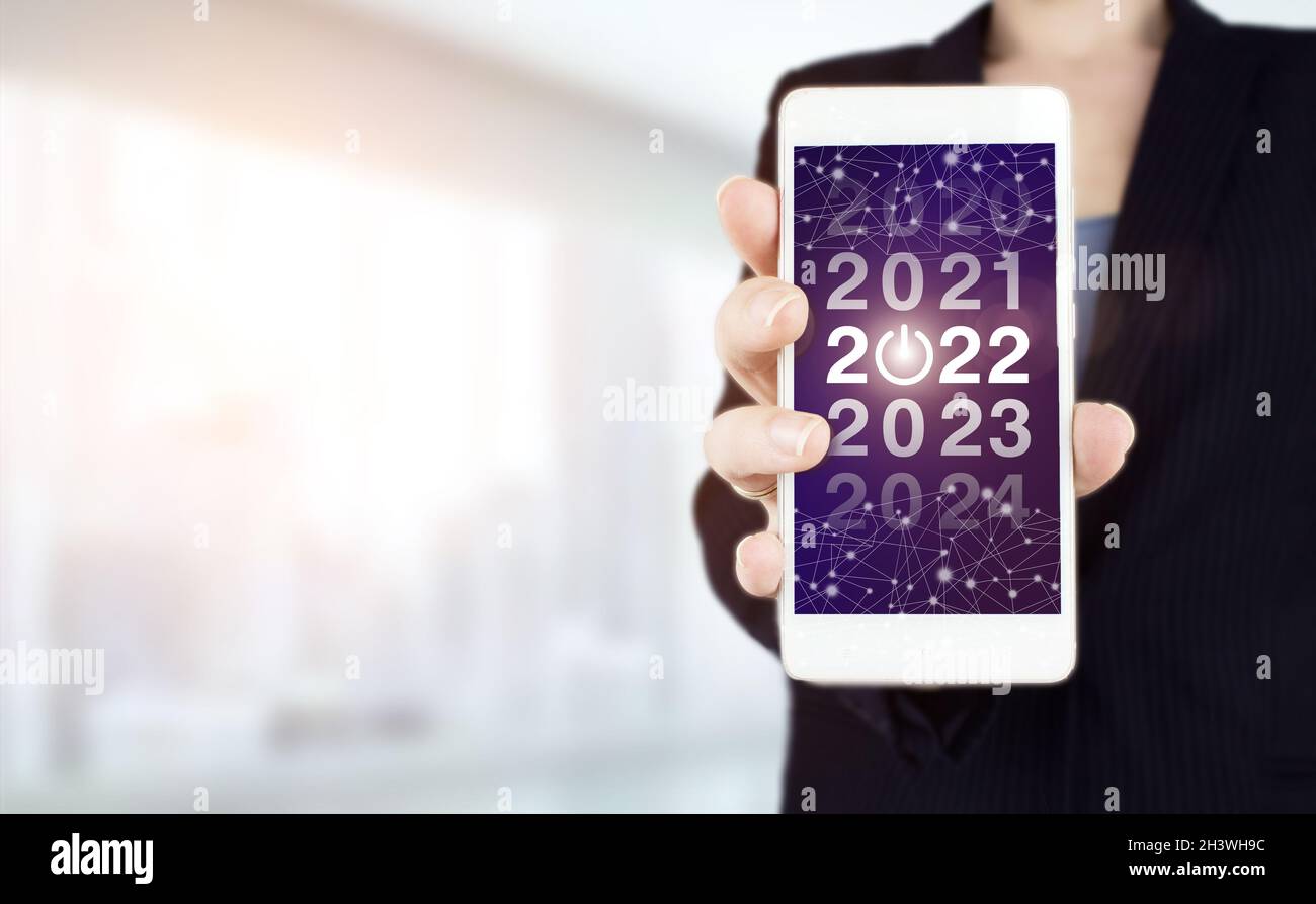 Concetto di nuovo anno. Smartphone bianco con hologram digitale 2022 su sfondo sfocato chiaro. Felice anno nuovo 2022 Foto Stock