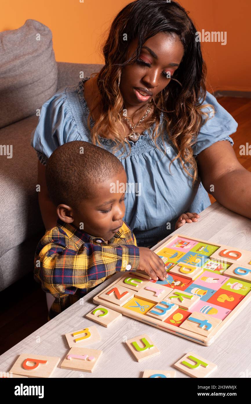 Bambino prescolare a casa con la madre, giocando con l'alfabeto puzzle con l'incoraggiamento della madre Foto Stock