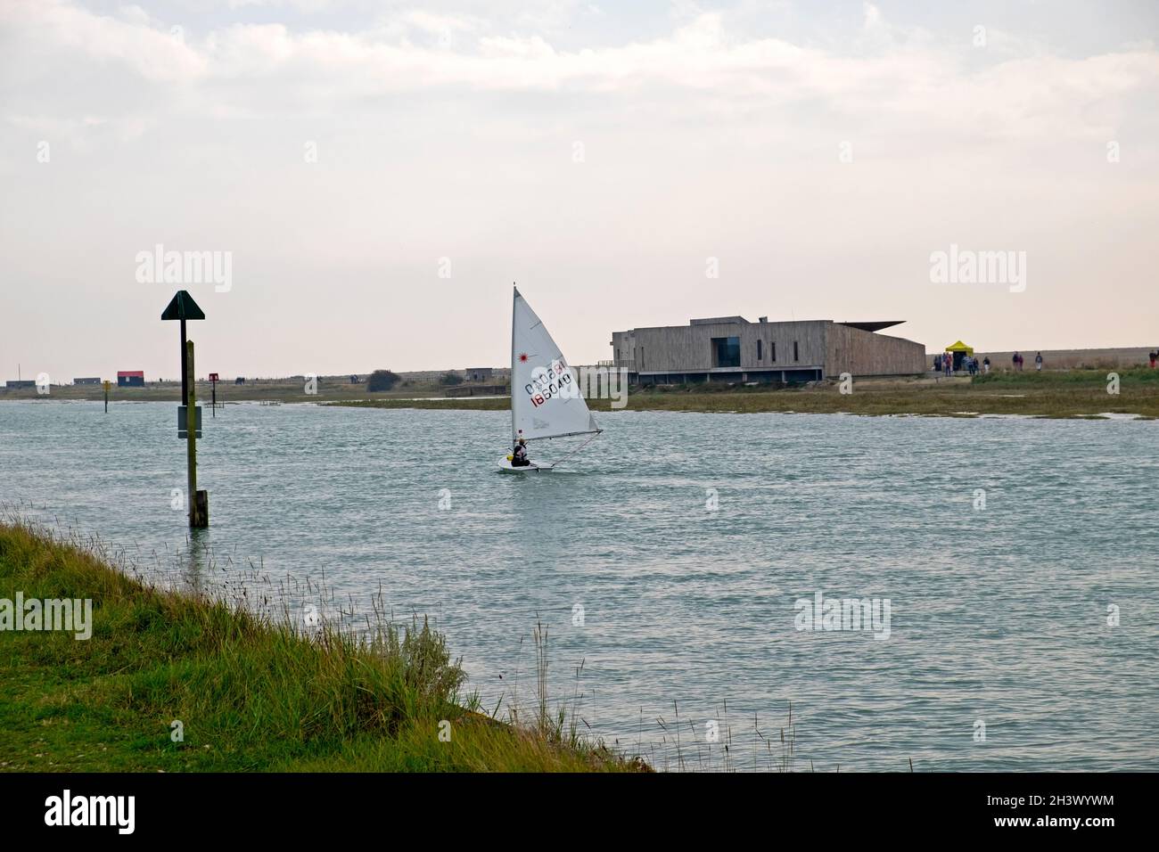 Piccola barca a vela che naviga oltre il Rye Discovery Centre sul Rother River Rye Harbour nel Sussex orientale Kent Inghilterra Regno Unito KATHY DEWITT Foto Stock