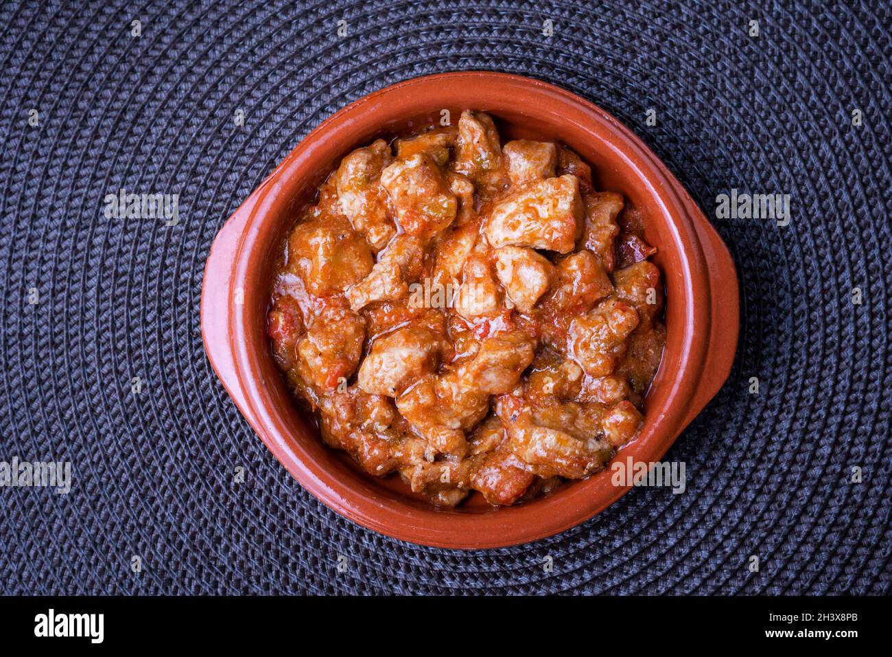 Piatto di argilla riempito di carne con pomodoro e isolato, su una tovaglia scura. Foto Stock